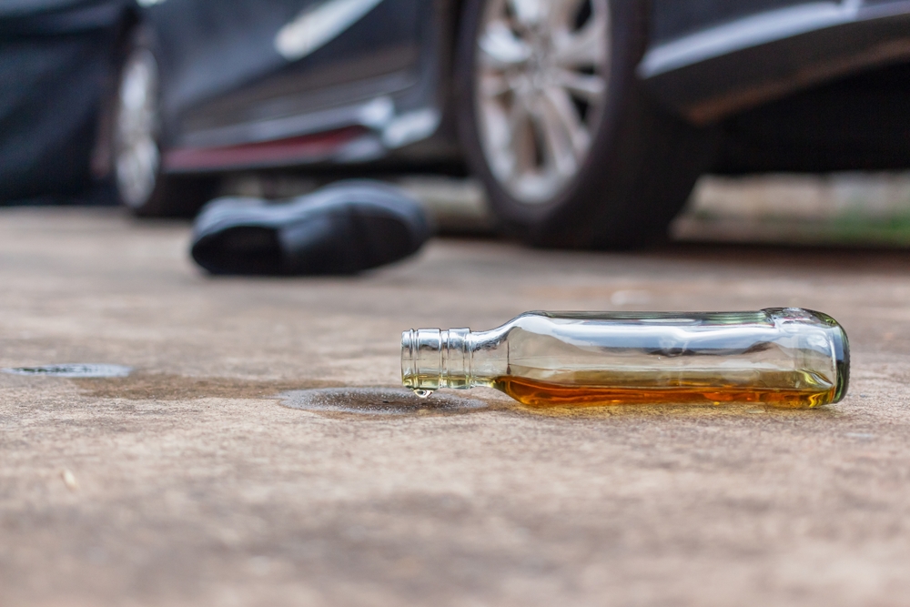 Empty alcohol bottle lying near a car, representing reckless or drunk driving behavior.